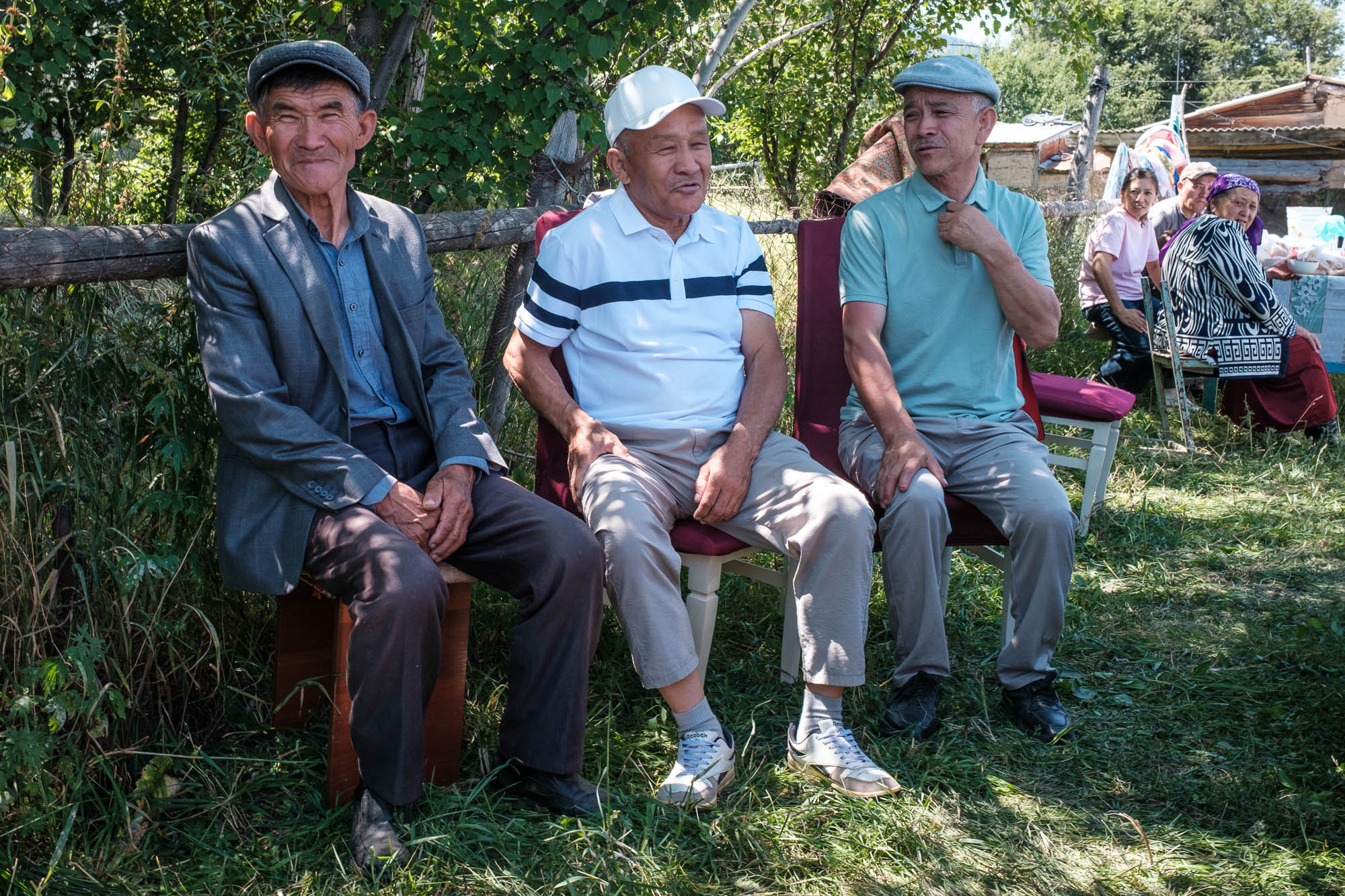 Drie mannen op stoelen in een tuin tijdens een dorpsfeest