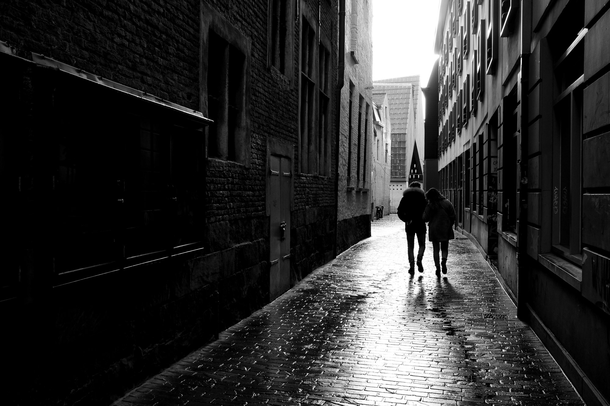 Koppel wandelt in tegenlicht door een Gents steegje